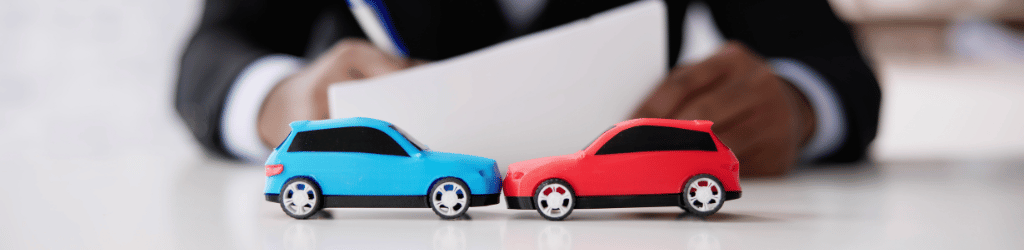 Lawyer going over documents at desk, two toy cars in simulated wreck on desk.
